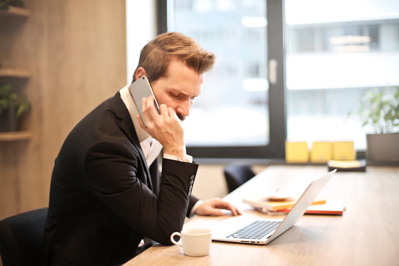 Man Having a Phone Call In-front of a Laptop

