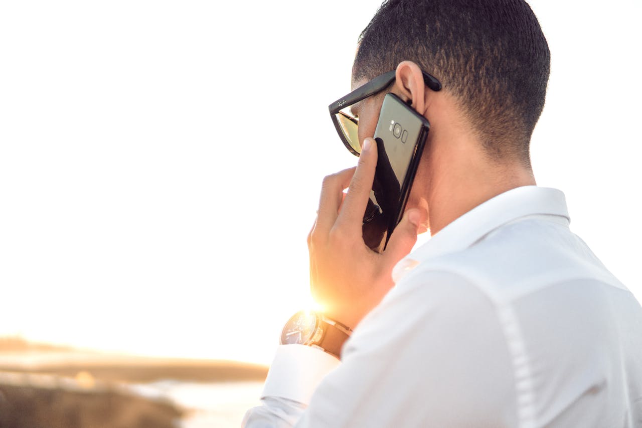 A man in White Collared Dress Shirt Talking to the Phone Using Black Android Smartphone
