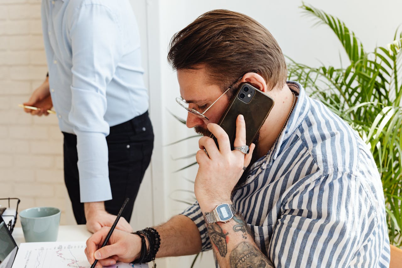 Man Writing While on a Phone Call