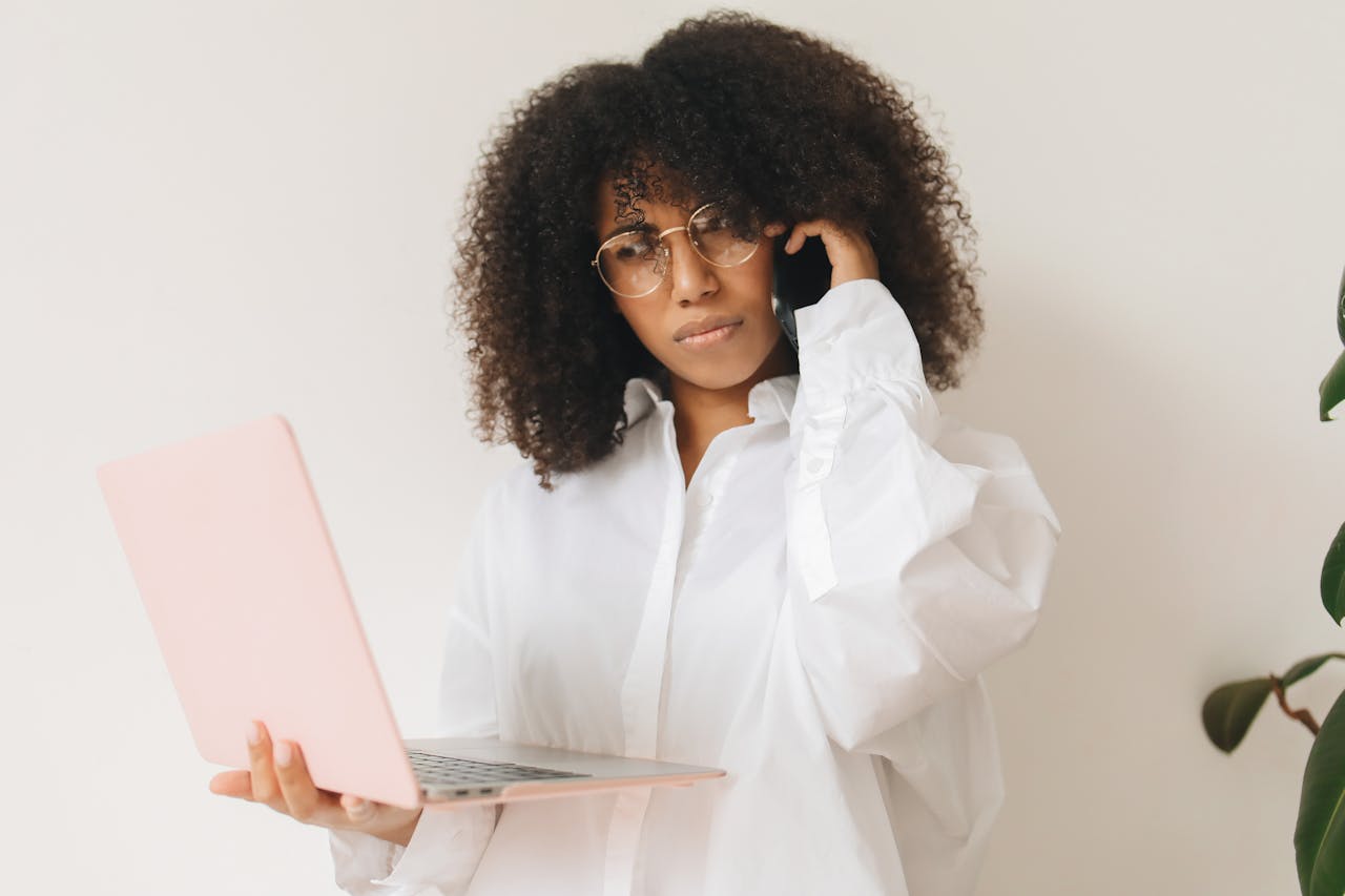  Woman in White Long Sleeve Shirt Holding Laptop While on Phone Call