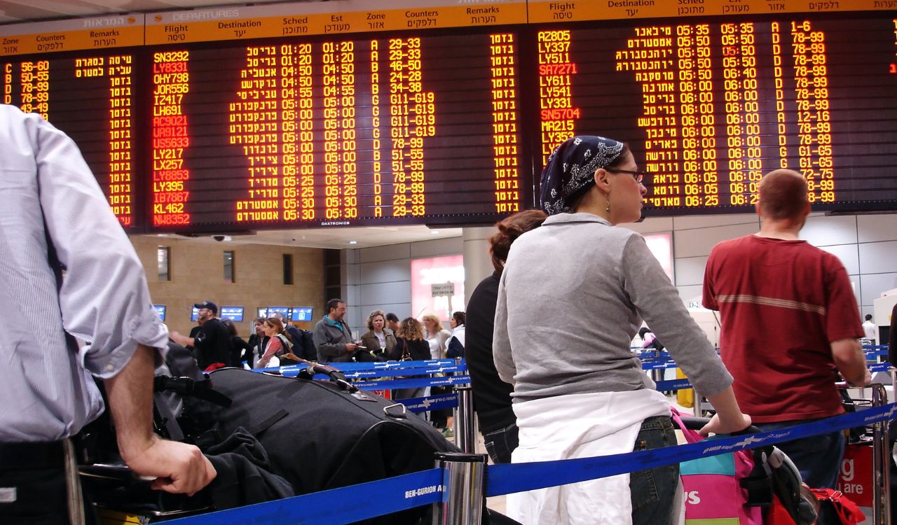 Air travelers stand under the flight information board in Tel Aviv airport terminal