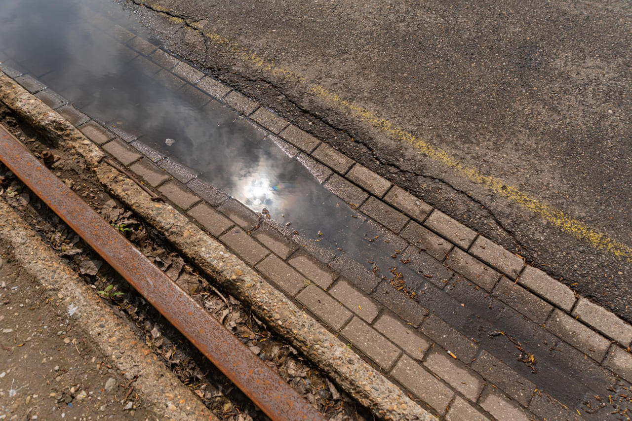 Oil streaks running along a driveway toward a storm drain.