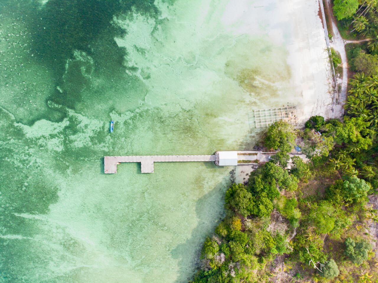 A shot of a lagoon from above, a couple walking along an overwater walkway,