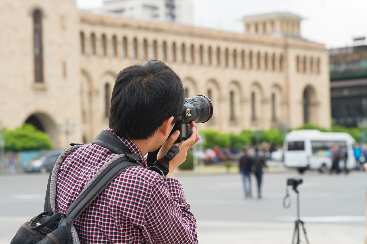 A traveler holding a camera near a restricted government building with visible “no photography” signage.
