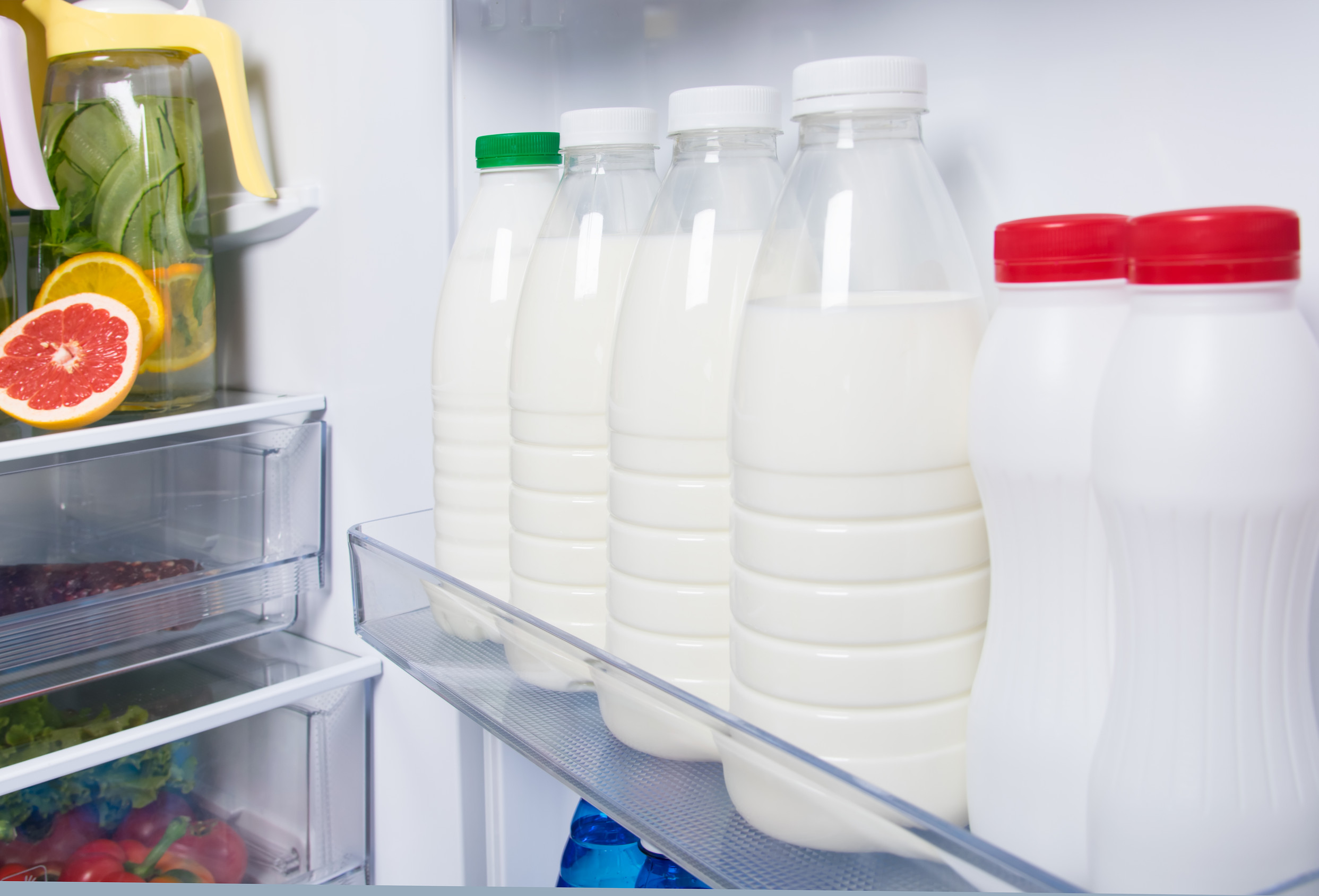 A bottle of raw milk beside standard pasteurized milk in a refrigerator case.
