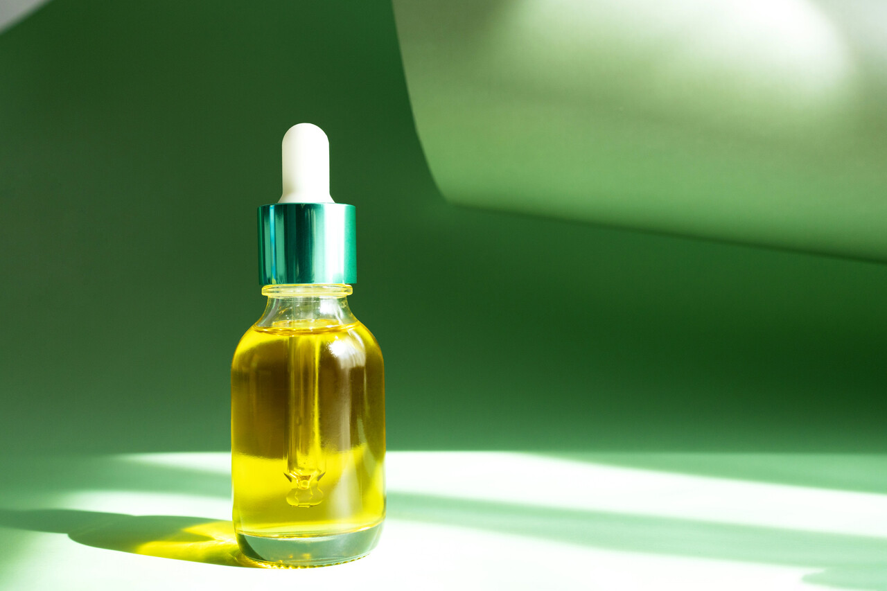 Transparent bottle with serum Mineral Oil or cosmetic product on a green background.