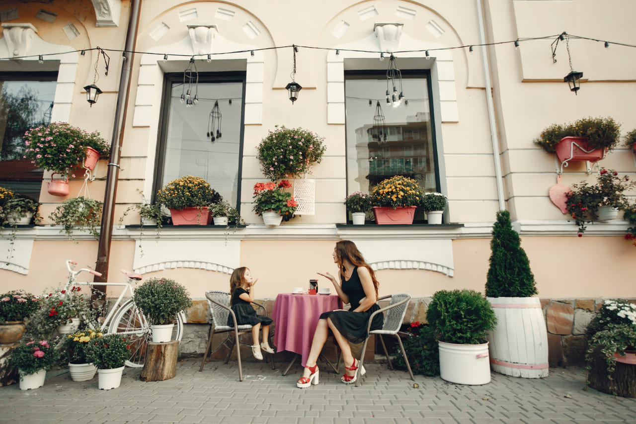 A warm café terrace or garden filled with flowers and soft colors that suggest comfort, charm and creative ease.