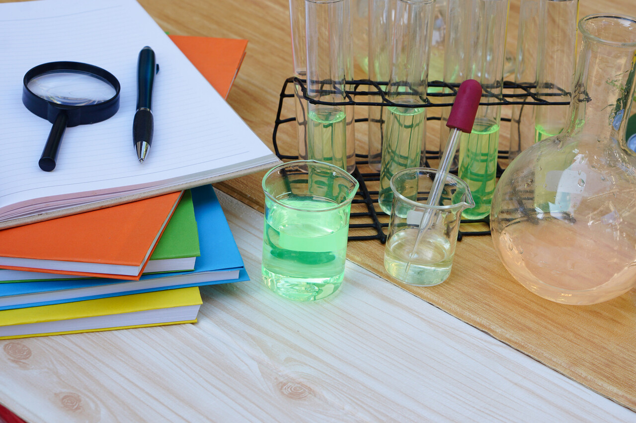 A classroom table with beakers, wires, small circuits, and a student mixing a simple experiment, all shot in a retro film style.