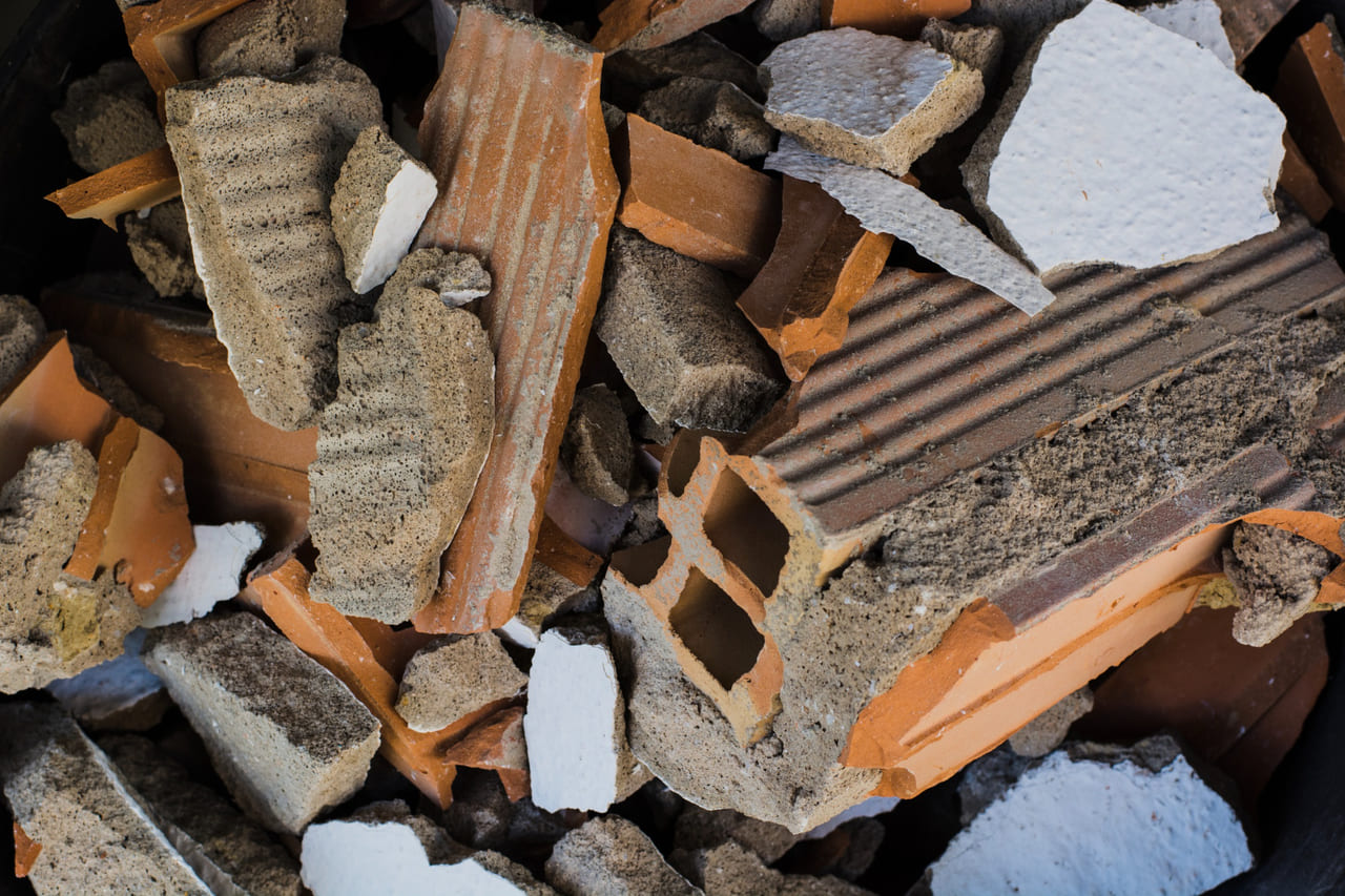 Broken drywall, cement pieces, shingles, and tiles abandoned on open land.