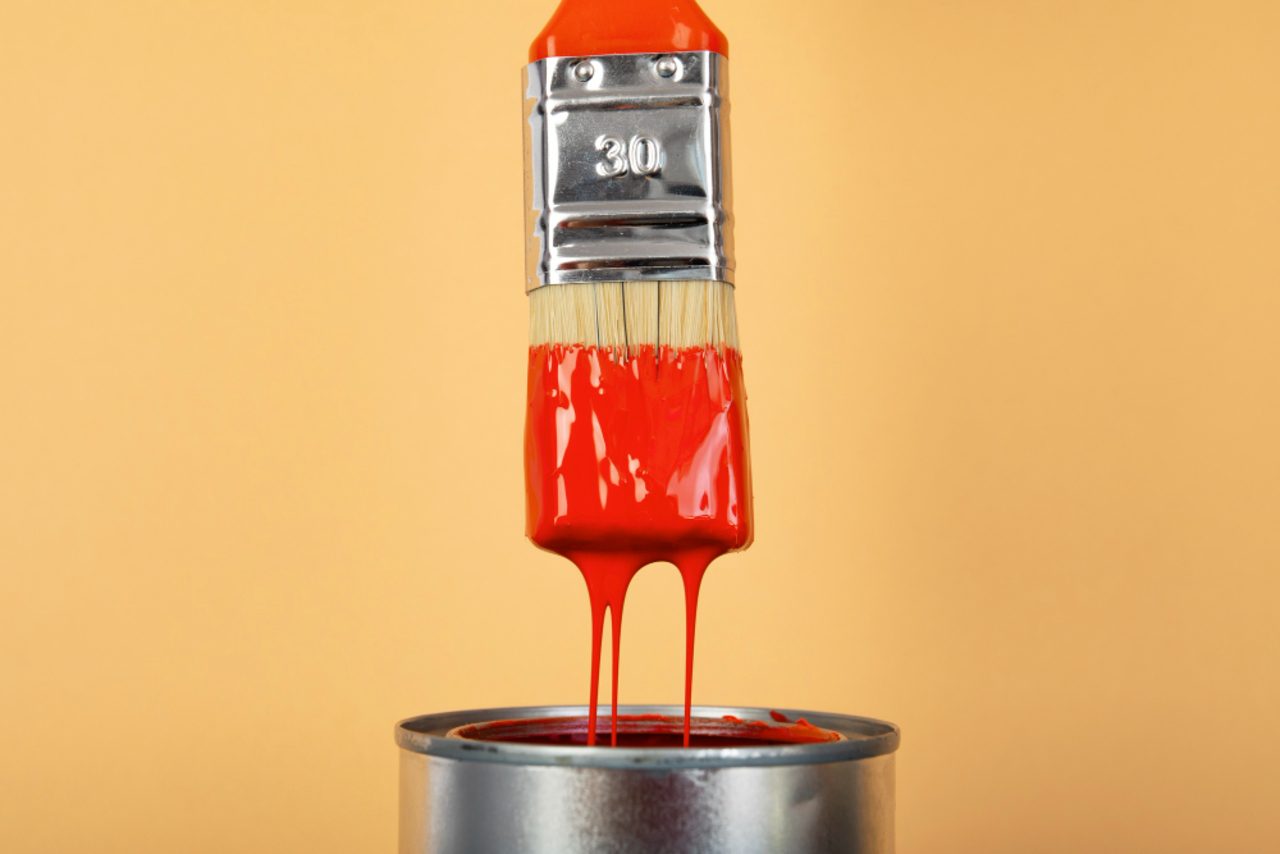 A close-up of a paintbrush being rinsed under a faucet with colored paint flowing toward a drain.