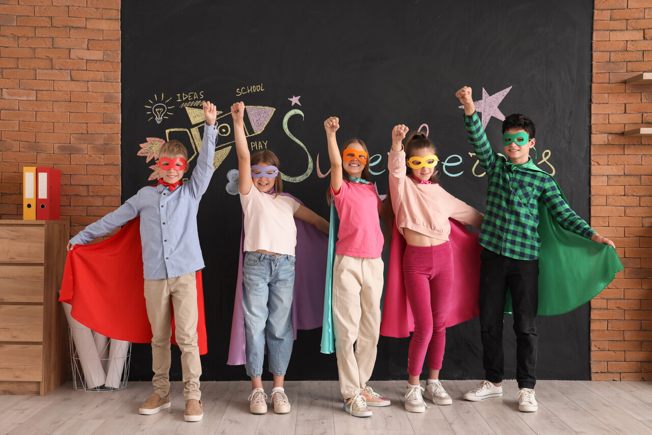 Students rehearsing on a small school stage with painted cardboard props in the background.