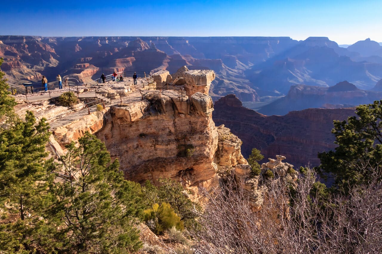 A daytime overlook view with visitors walking the rim trail or gathering at a popular viewpoint.