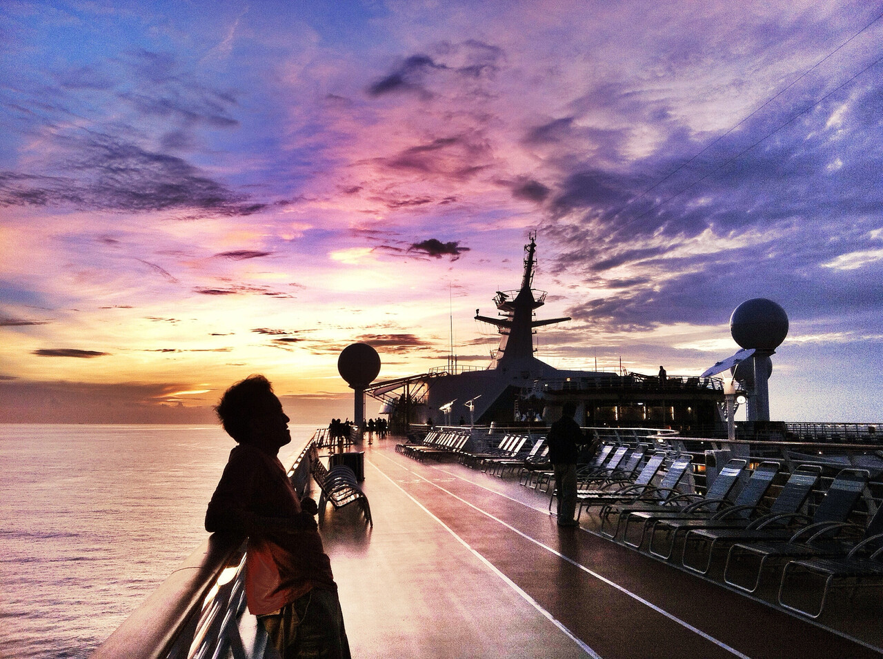 A quiet ship deck at dusk with sailors avoiding noise as wind gathers on the horizon.