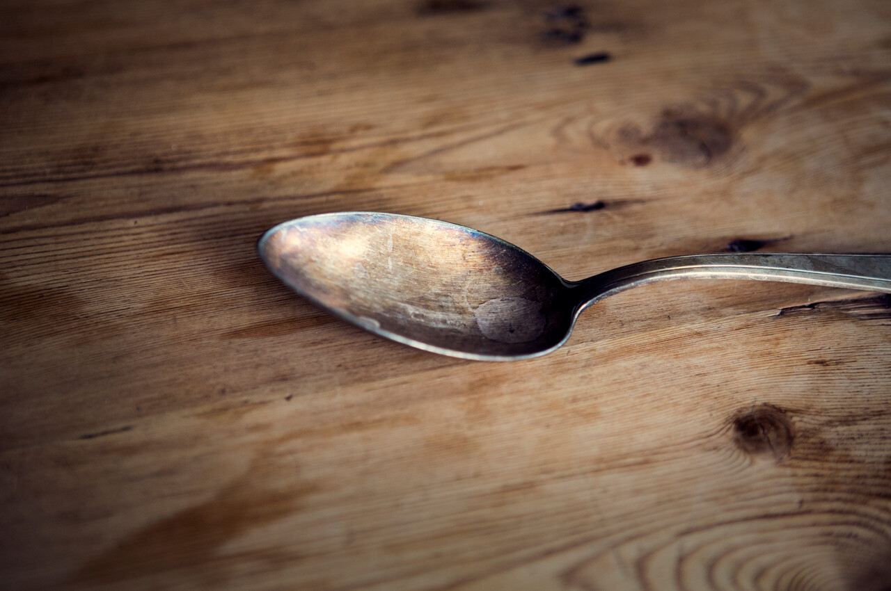 A metal spoon lying on a wooden floor beside packed luggage near a hearth.