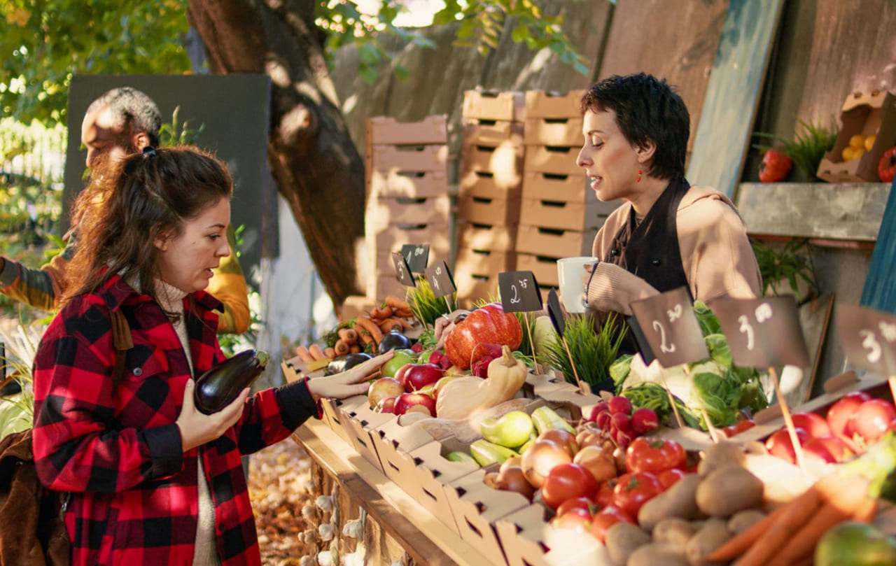 A wide shot of a farmers market stall with various packaged foods, labels, and fresh produce arranged together.