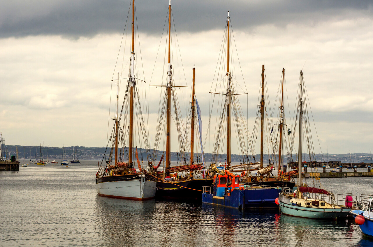 A seventeenth-century harbor scene with ships waiting at the docks under an overcast sky.