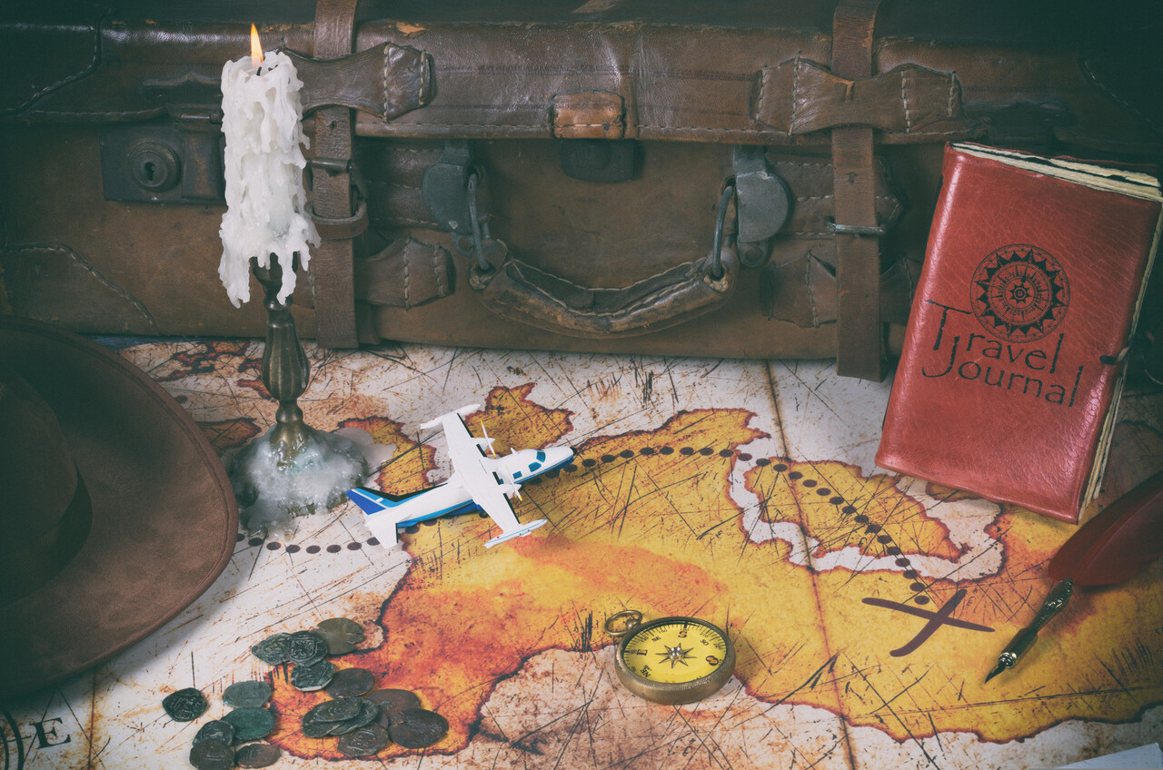 A vintage map spread across a wooden table with an old compass, faded tickets and a candle casting a soft glow.