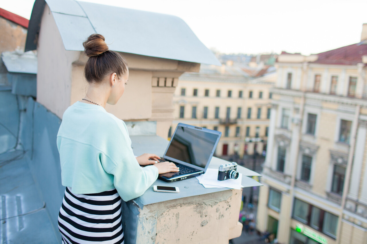 A couple working on laptops at a sunny balcony overlooking tiled roofs