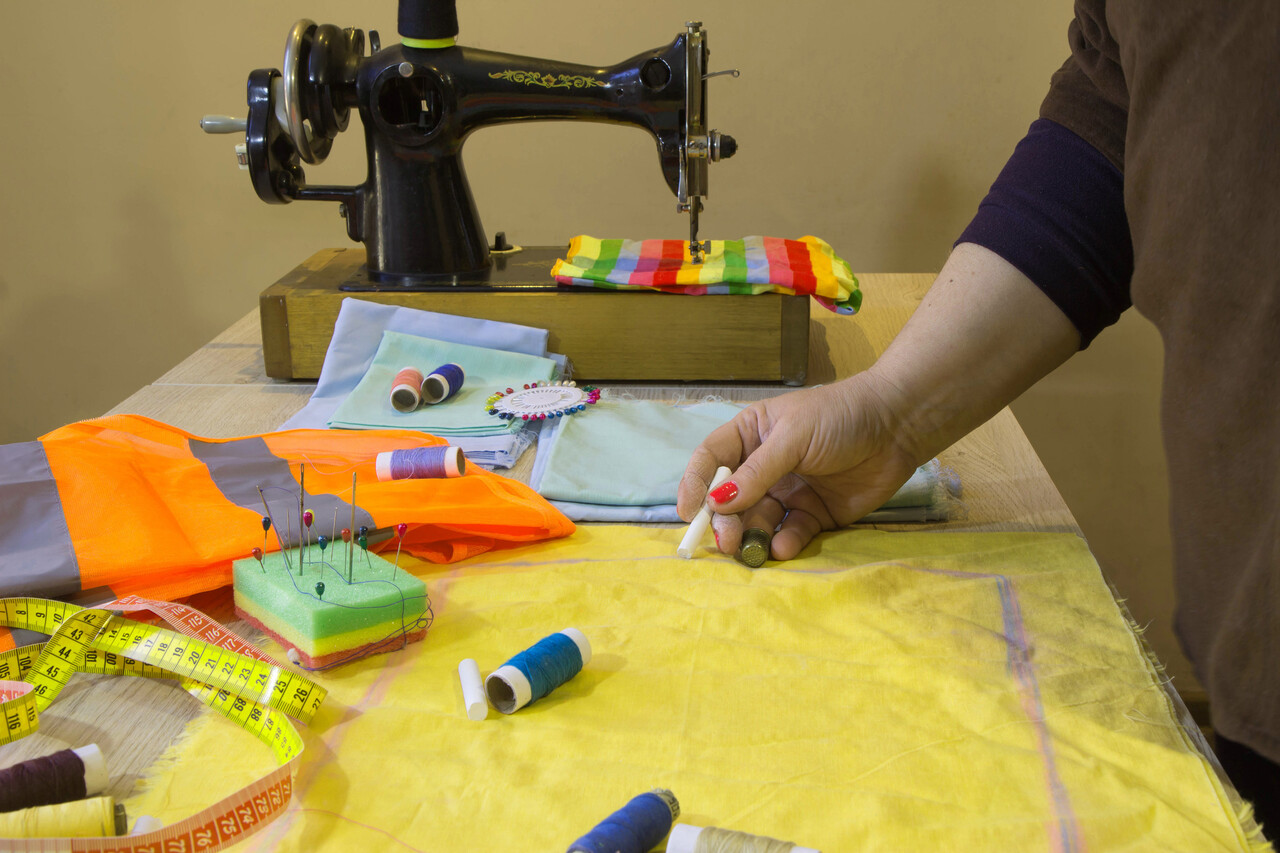 A sewing machine on a school table with fabric scraps and a student learning stitches, styled like a 1970s home-ec classroom.