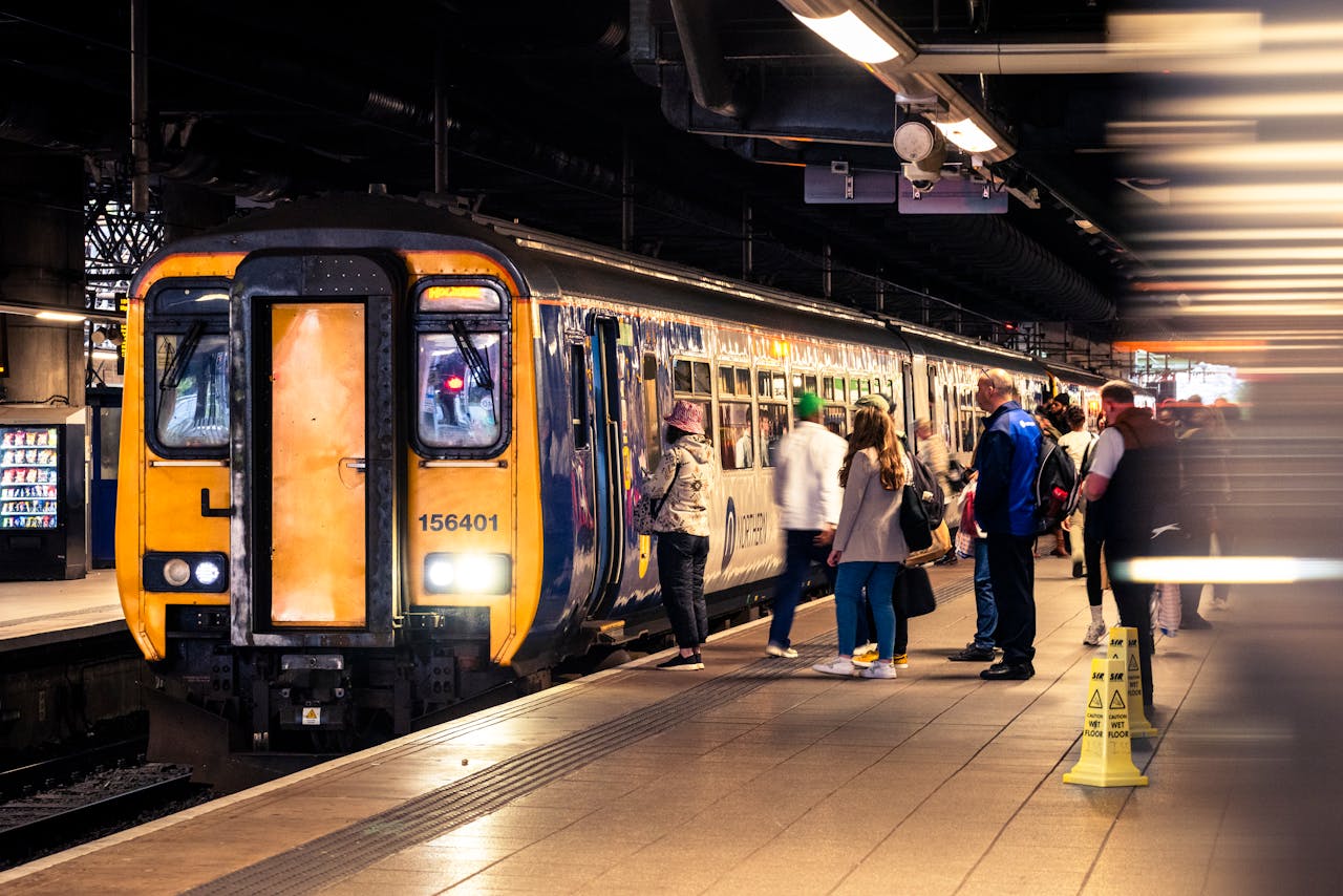 A busy UK rail station showing passengers forming an orderly queue at a platform entrance.