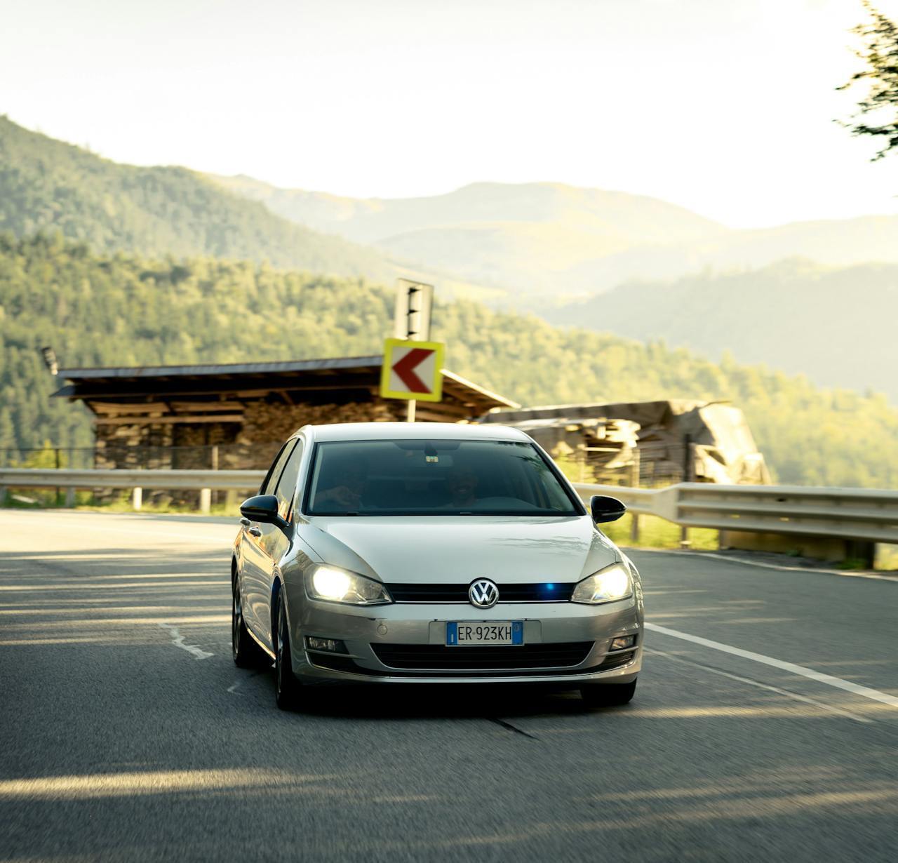A Scandinavian rural road in bright daylight with cars driving with headlights on.