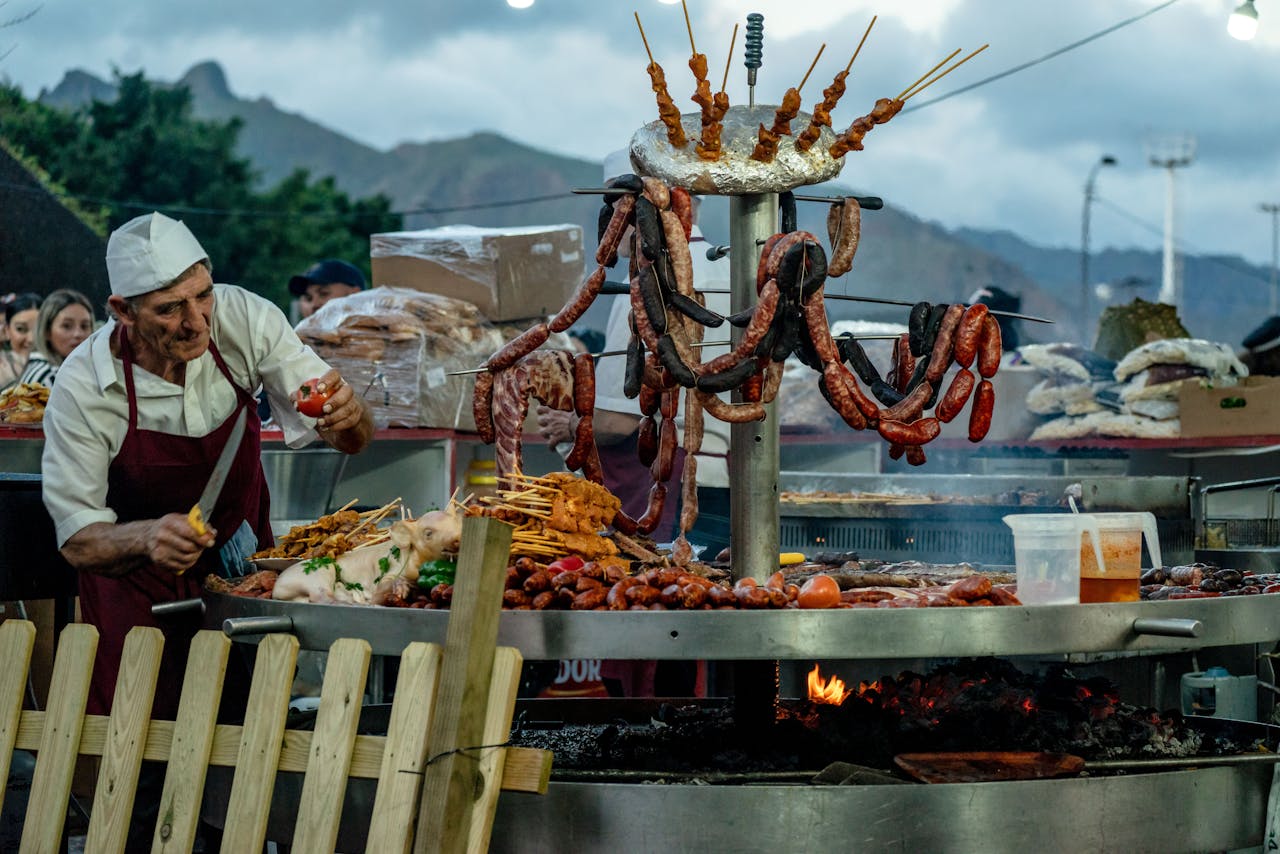 A street vendor grill with meat skewers under a shaded canopy.