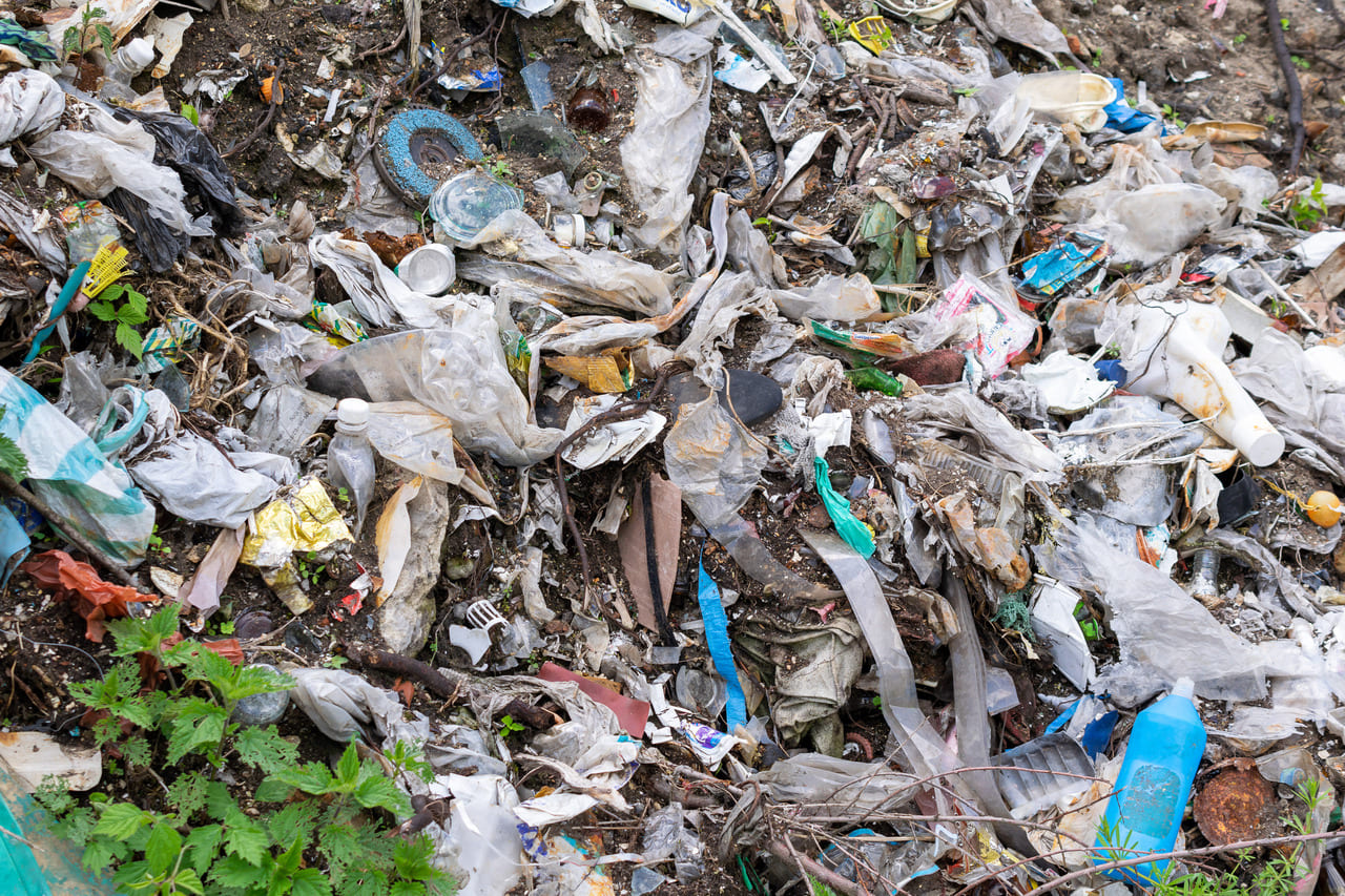 A shallow backyard pit with plastic containers and debris partially covered by soil.