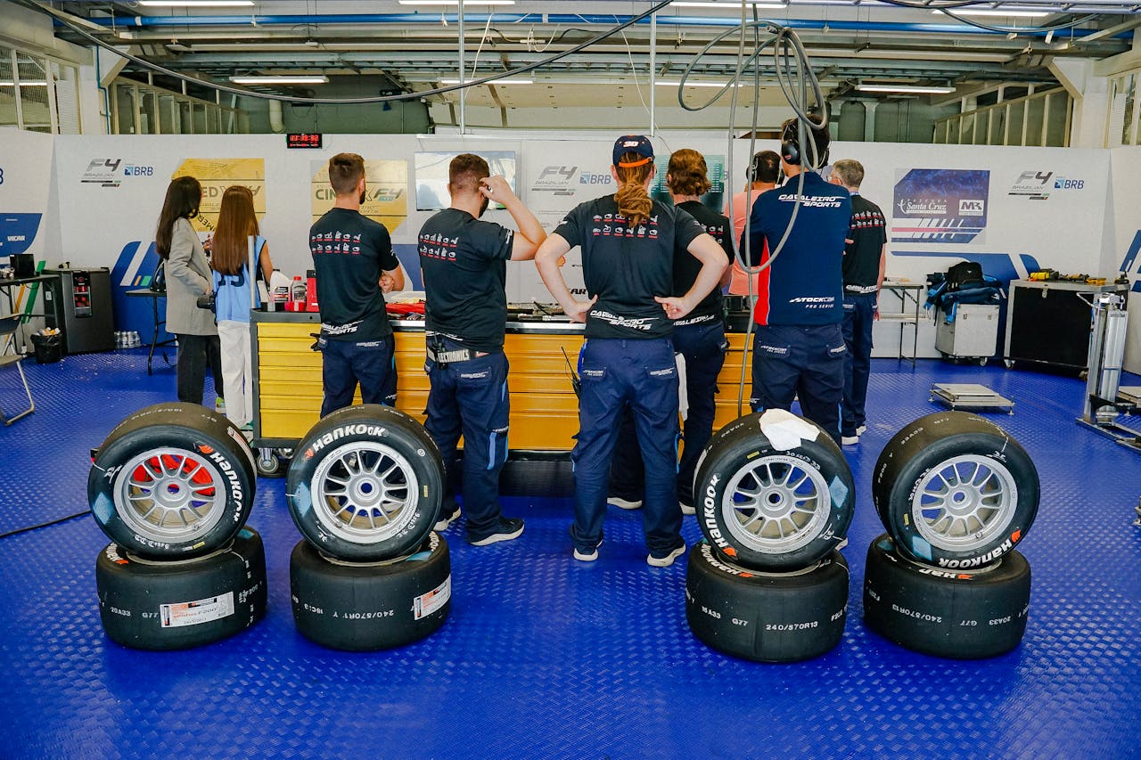 Set of worn tires stacked next to a new tire, highlighting tread differences and showing a mechanic preparing to replace tires on a vehicle.