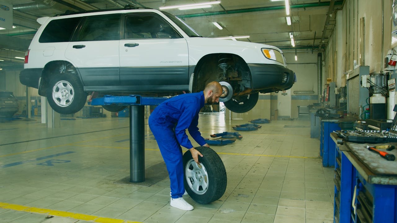 Technician using a wheel alignment machine while a car is lifted in a garage, showing equipment and tools for tire rotation and alignment.