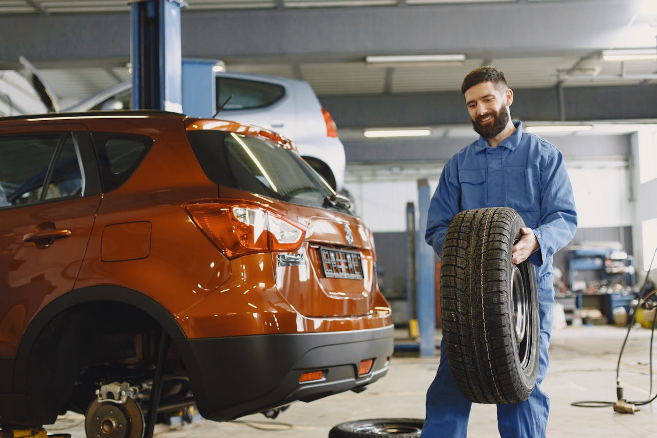 Mechanic inspecting a car tire on a lift, pointing to the TPMS sensor on the valve stem, ready for testing or replacement.