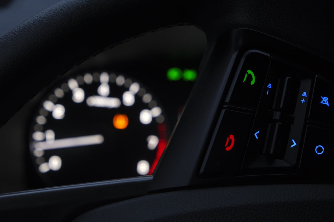 Driver pressing the TPMS reset button on a car dashboard, with the tire pressure warning light visible on the instrument panel.