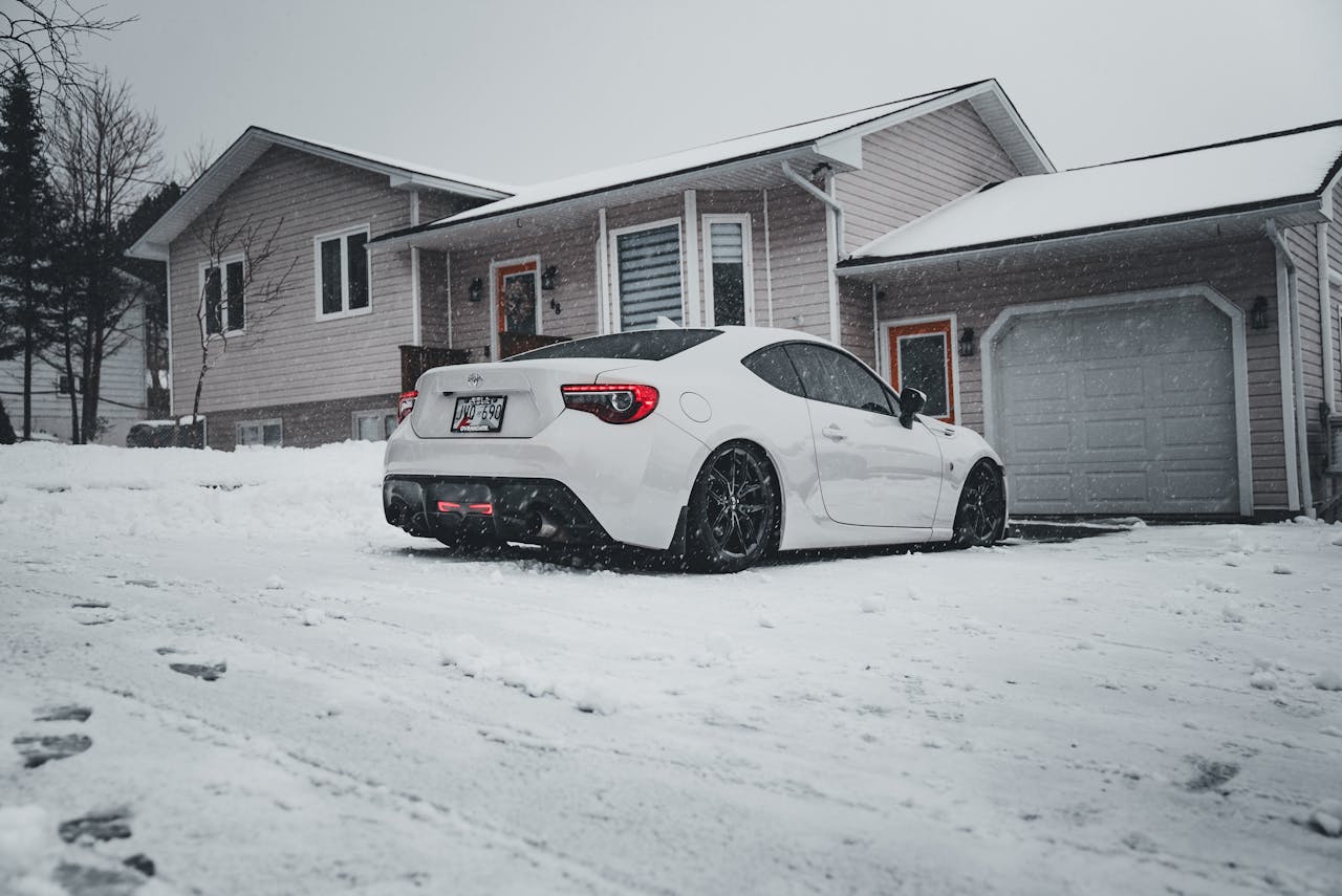 Morning scene of a car parked in a snowy driveway with frost on the tires, illustrating how cold weather can affect tire pressure.