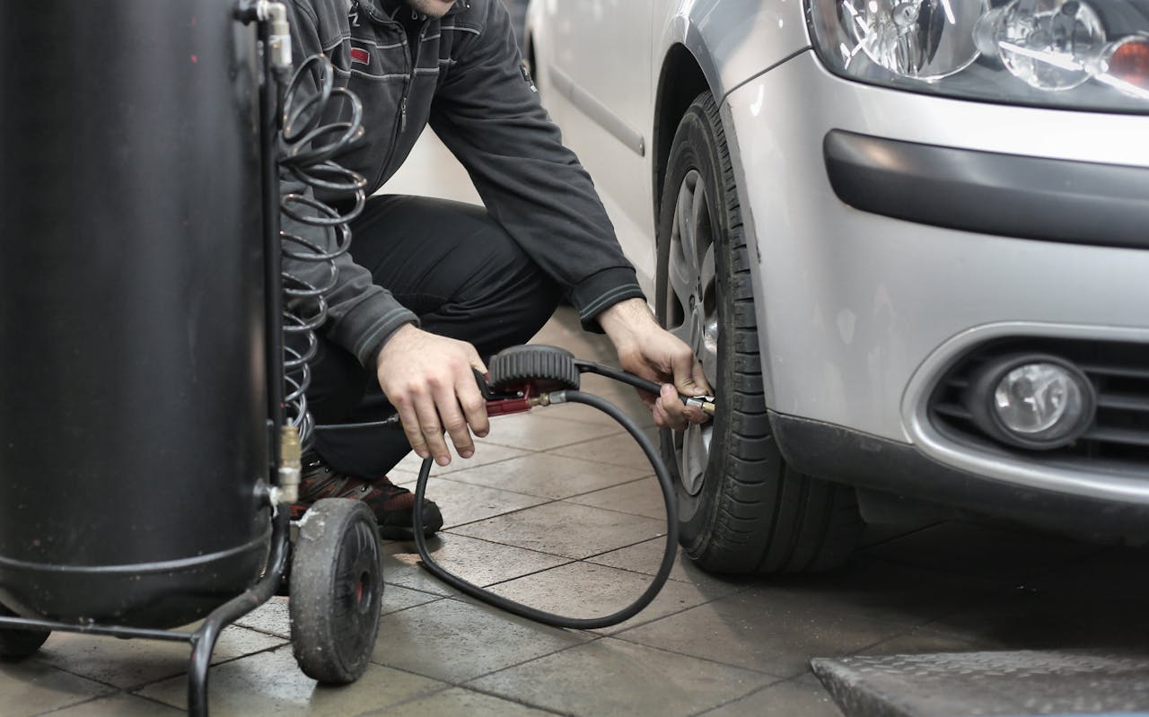 Close-up of a driver using a digital tire pressure gauge on a car tire, showing the reading while sunlight highlights the tire tread.
