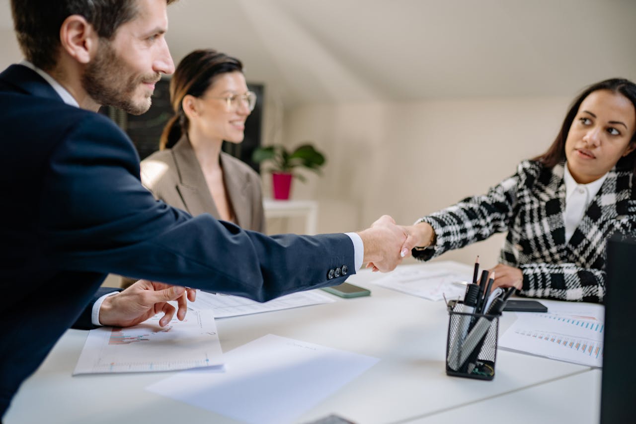 A business interaction where a junior employee offers a handshake before a senior executive, illustrating the importance of hierarchy awareness.