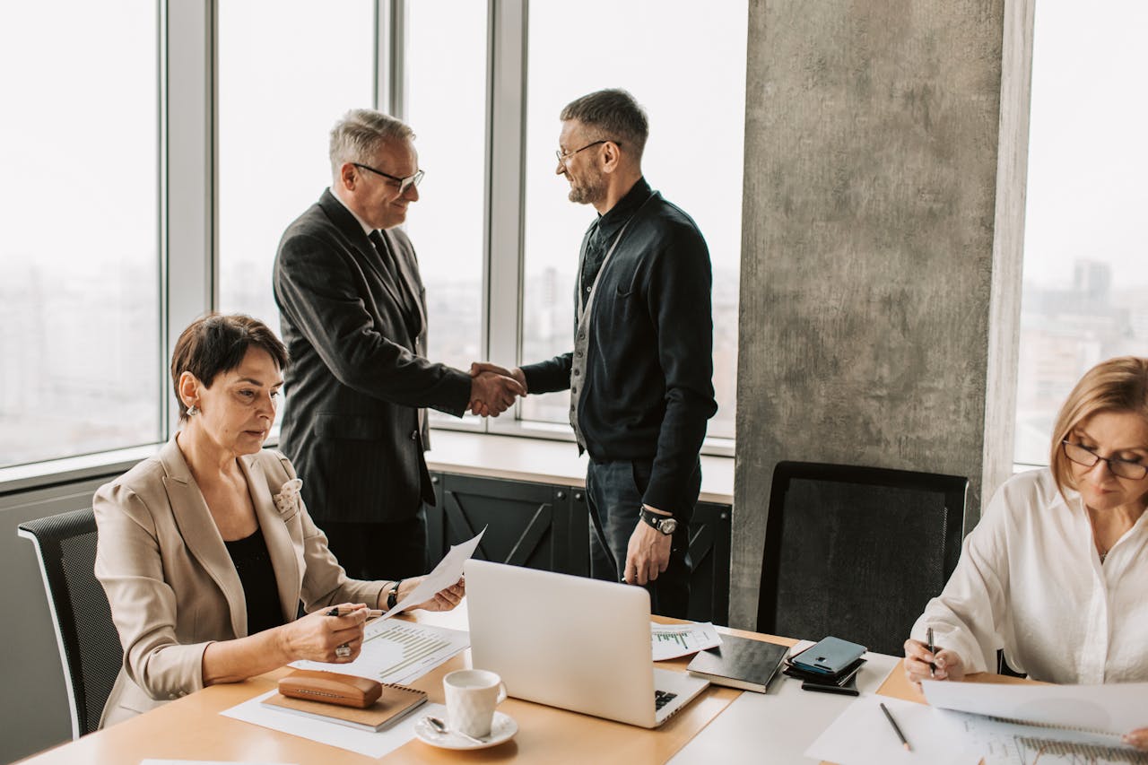 Two professionals greeting, one bowing slightly while the other only offers a handshake, showing differing cultural expectations.