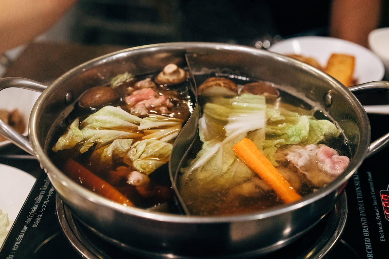 A simmering pot of golden bone broth with herbs and vegetables on a stovetop.