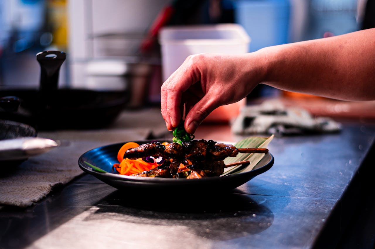 A chef assembling a dish using partially prepared ingredients in a restaurant kitchen.
