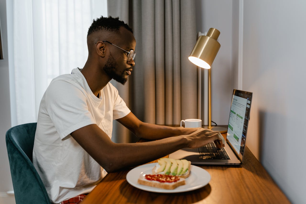 Person working on a laptop at a home desk with distractions like cluttered papers and a coffee cup