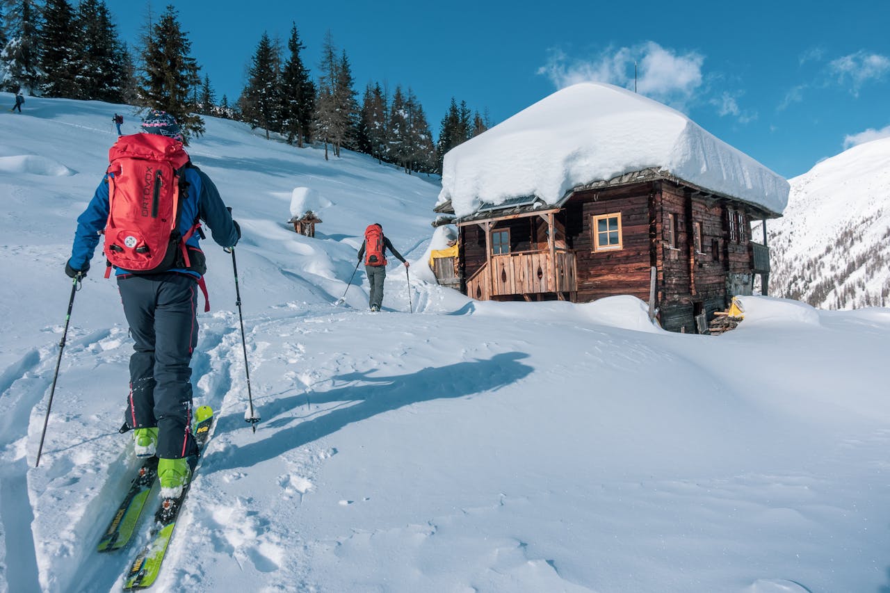 Person hiking on a snowy trail wearing winter gear with a bright blue sky