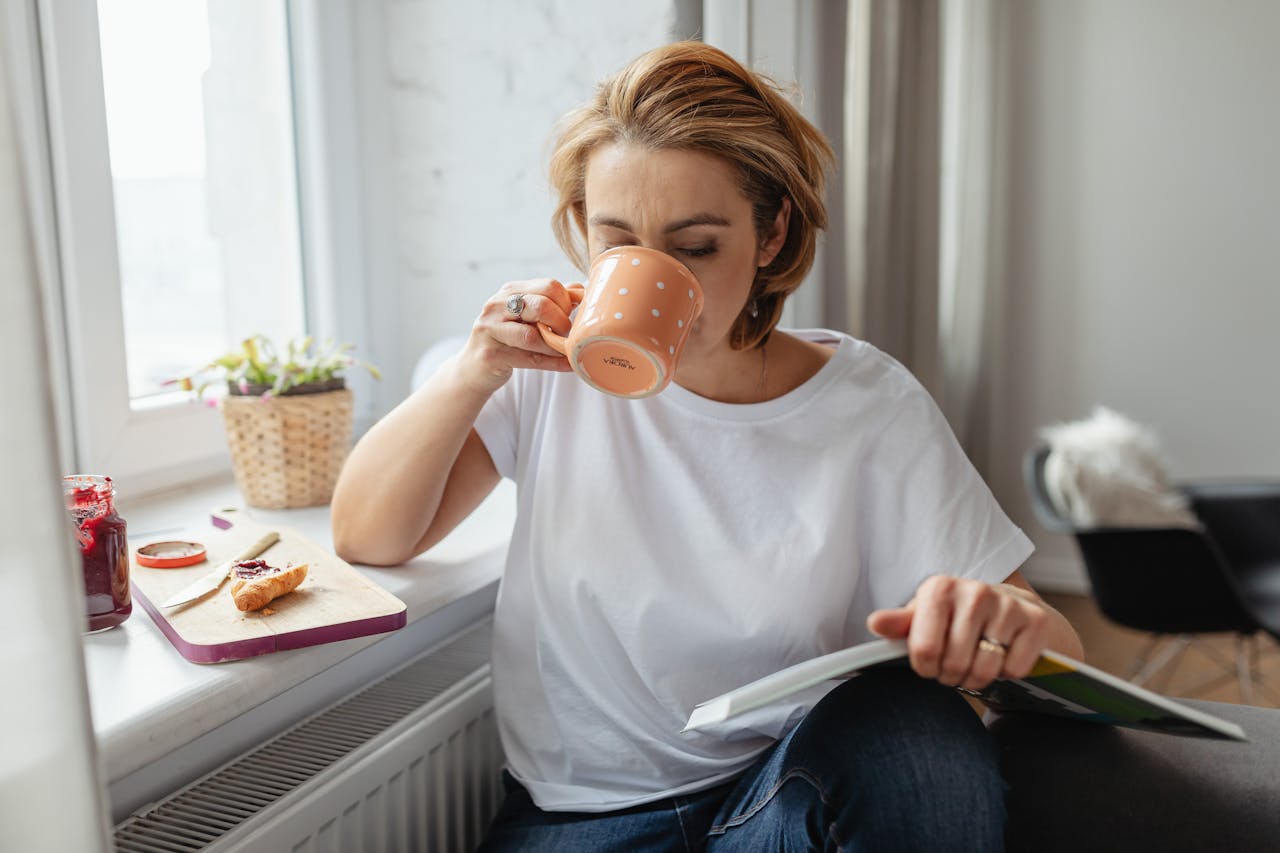 Person sipping coffee at sunrise while journaling near a window