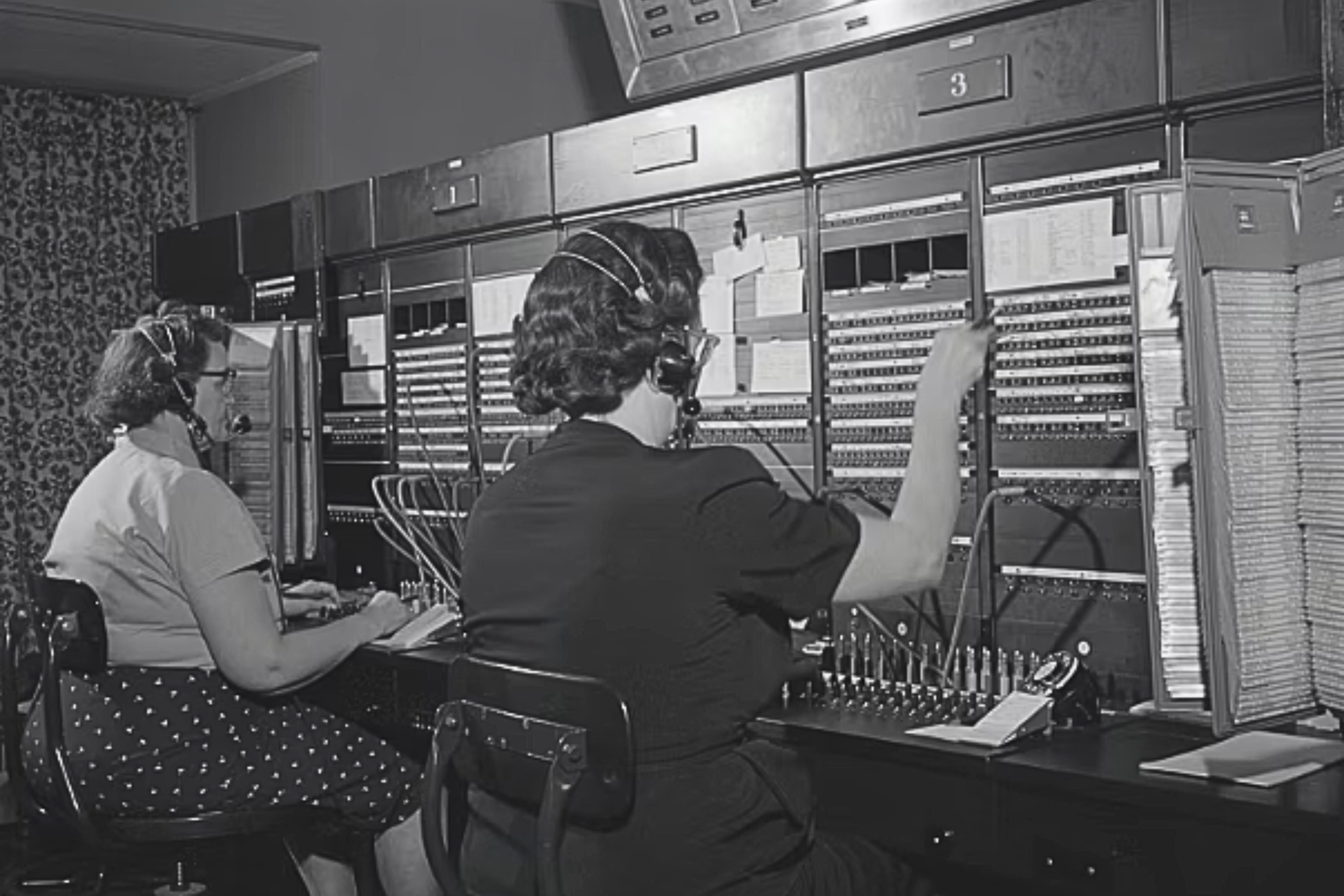 Female operators using headsets and speaking French and English while connecting calls on a military switchboard