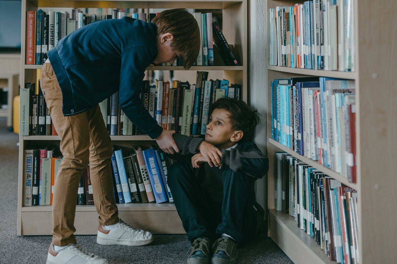 Two boys sitting and standing near a bookcase showing emotional pressure and concern