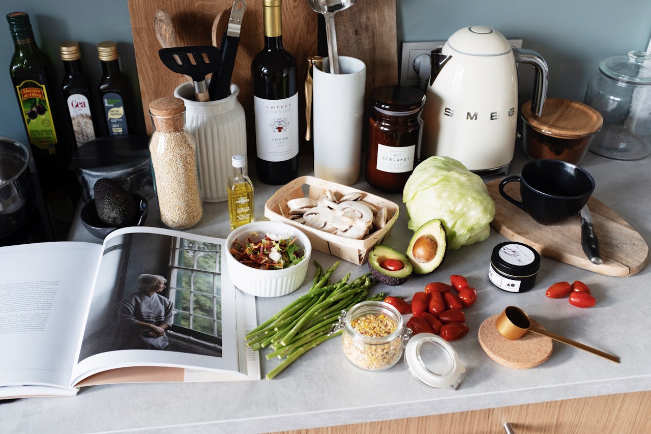 A kitchen countertop displaying spices, jars of sauces, milk, fresh herbs, nut butter, coffee beans, and batteries, highlighting everyday household items that expire quickly.