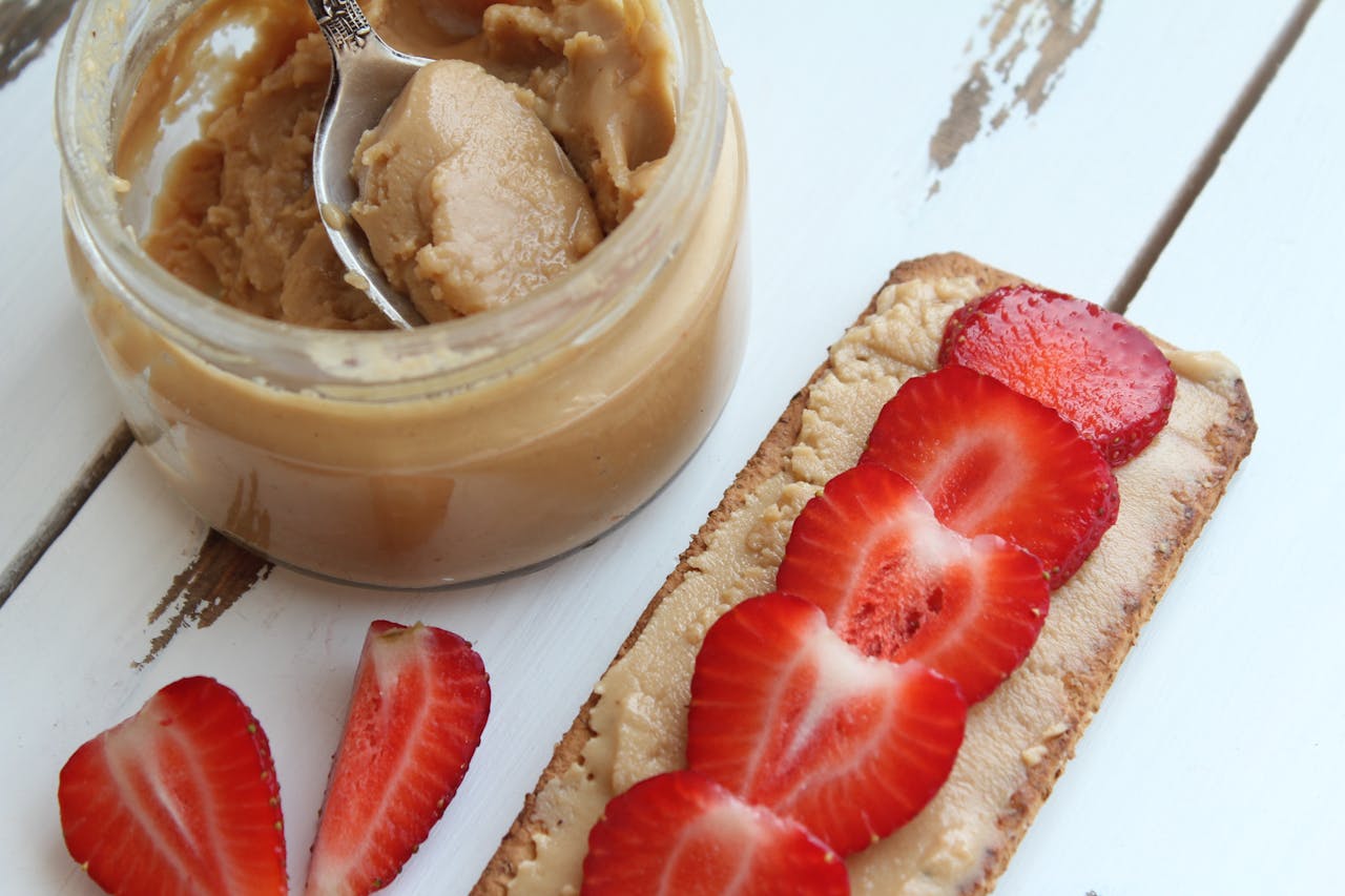 Open jar of peanut butter with a spoon and fresh almonds