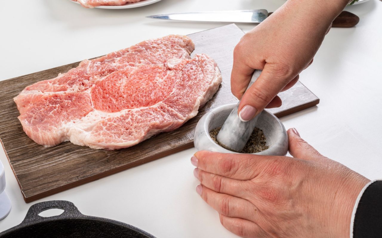 Steak seasoned with salt and pepper resting on a countertop before cooking