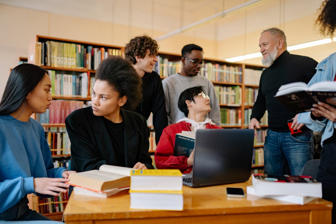 Small group sitting around a table in a cozy library or café discussing books with open paperbacks and notebooks.